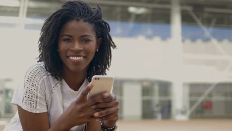 Happy-beautiful-woman-holding-smartphone-and-looking-at-camera.